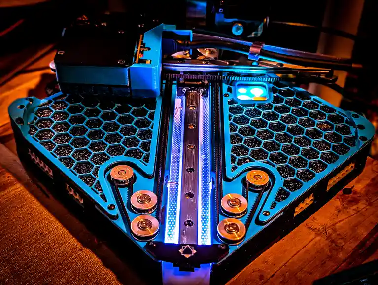 A custom-built 3D printer with a blue, hexagonal-patterned frame and glowing blue LED strips is shown on a wooden surface…