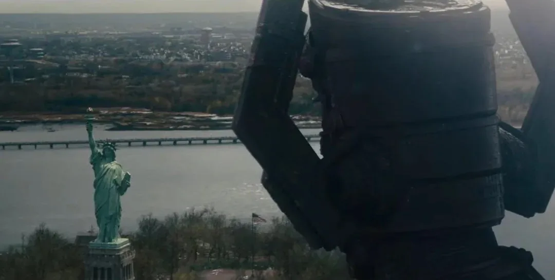 A close-up shot of a large, dark, mechanical arm or claw dominates the foreground, partially obscuring the view. In the…