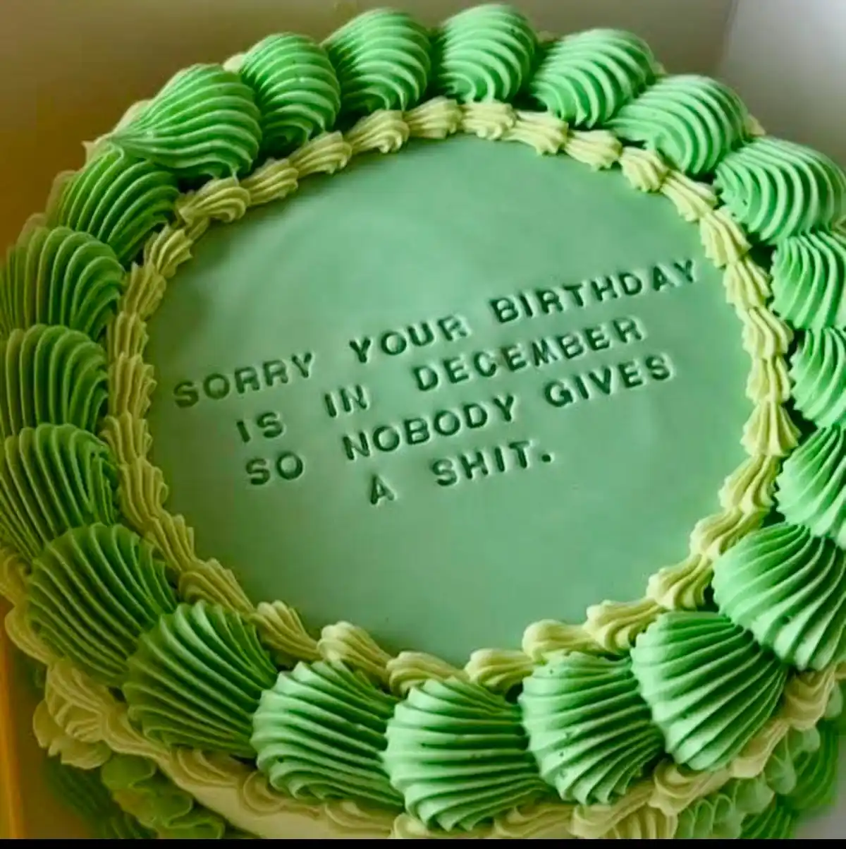 A close-up of a round birthday cake with green and light green frosting piped in a decorative border. The cake's smooth…