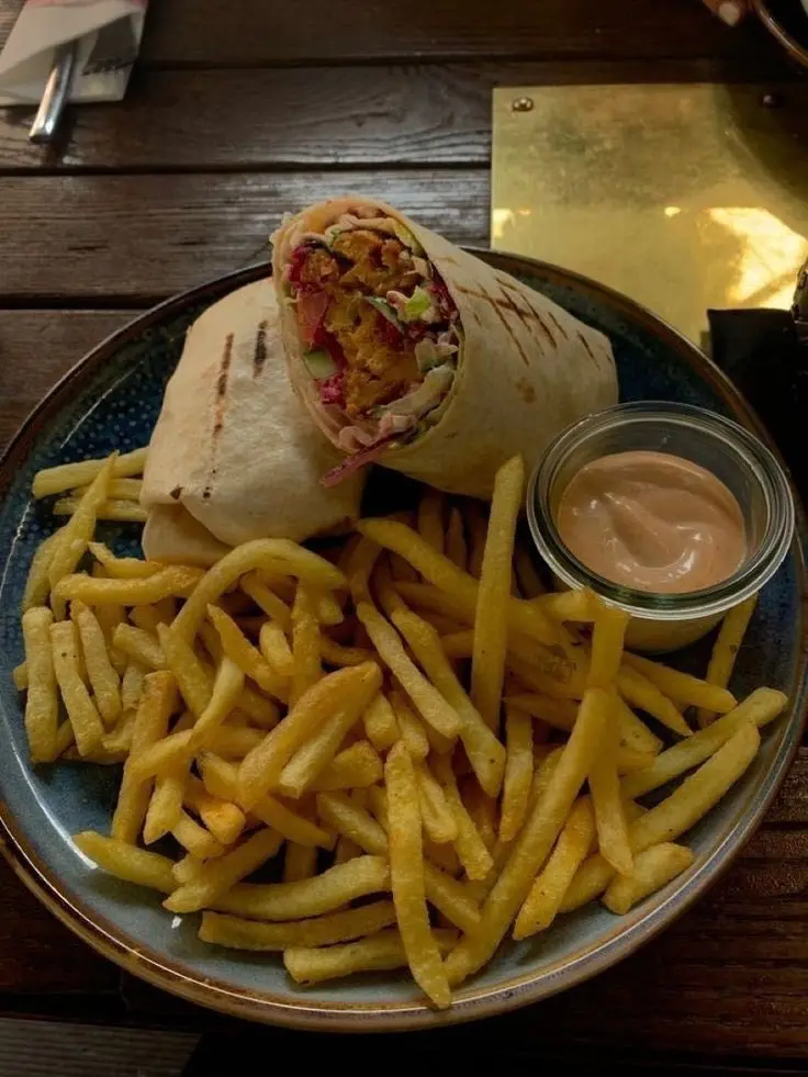 A plate of food featuring a large wrap, sliced in half to show its colorful fillings, served with a generous pile of golden…
