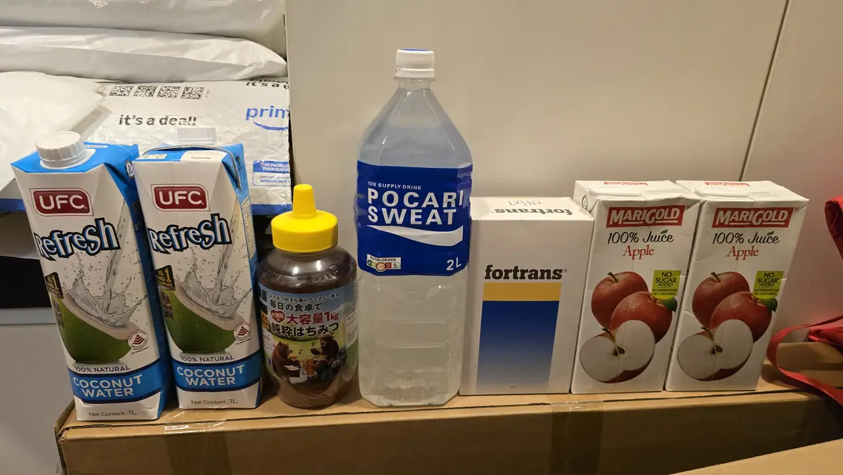 A lineup of beverages and health products on a cardboard box includes two UFC coconut water cartons, a bottle of Pocari…