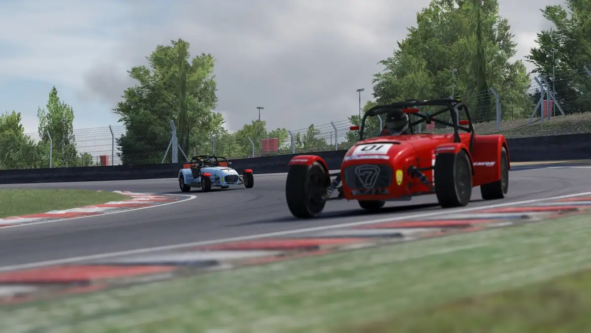 Two open-wheel race cars, one red and one light blue, are shown on a racetrack corner with red and white curbing. The red…