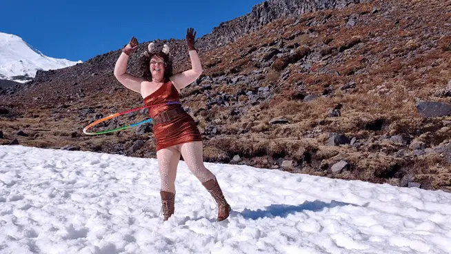 A woman in a red outfit and animal ears stands in snowy mountains, hula hooping with multiple hoops. The sequence shows her…