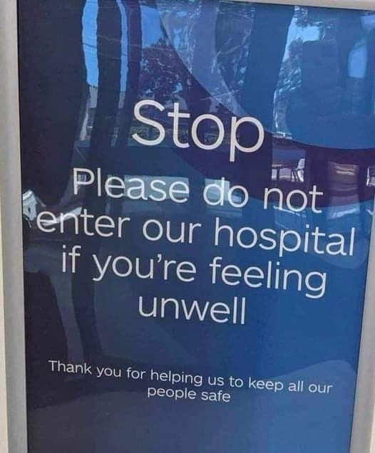A blue hospital sign with white text reads 'Stop Please do not enter our hospital if you're feeling unwell Thank you for…