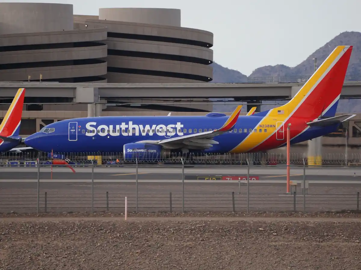 A blue Southwest Airlines Boeing 737 with red, yellow, and blue tail livery is parked on an airport tarmac in front of a…