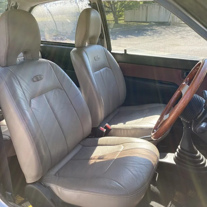The image shows the interior of a car, focusing on two light-colored leather front seats with visible stitching and…