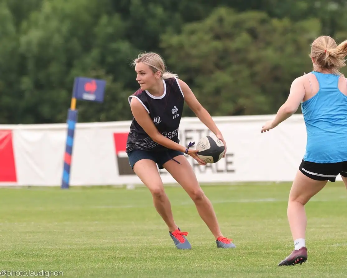 A female rugby player in a dark blue training jersey with 'FFR' and 'SOCIETE GENERALE' logos holds a rugby ball, looking…