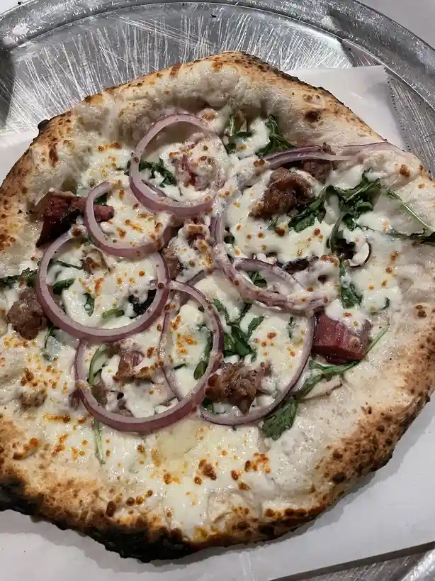 A close-up photo of a freshly baked pizza with a golden-brown crust, topped with melted white cheese, red onion rings, green…