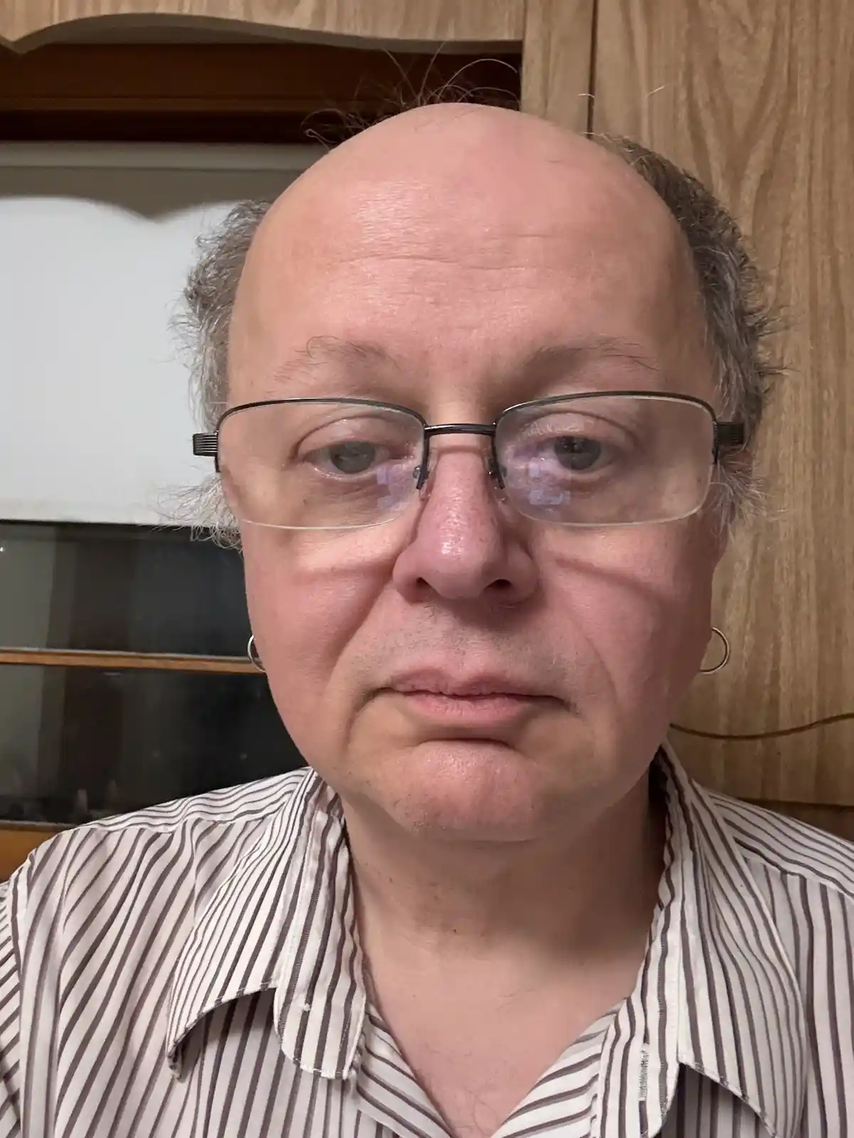 A close-up photo of a middle-aged man with a balding head, wearing glasses and a striped shirt, looking directly at the…