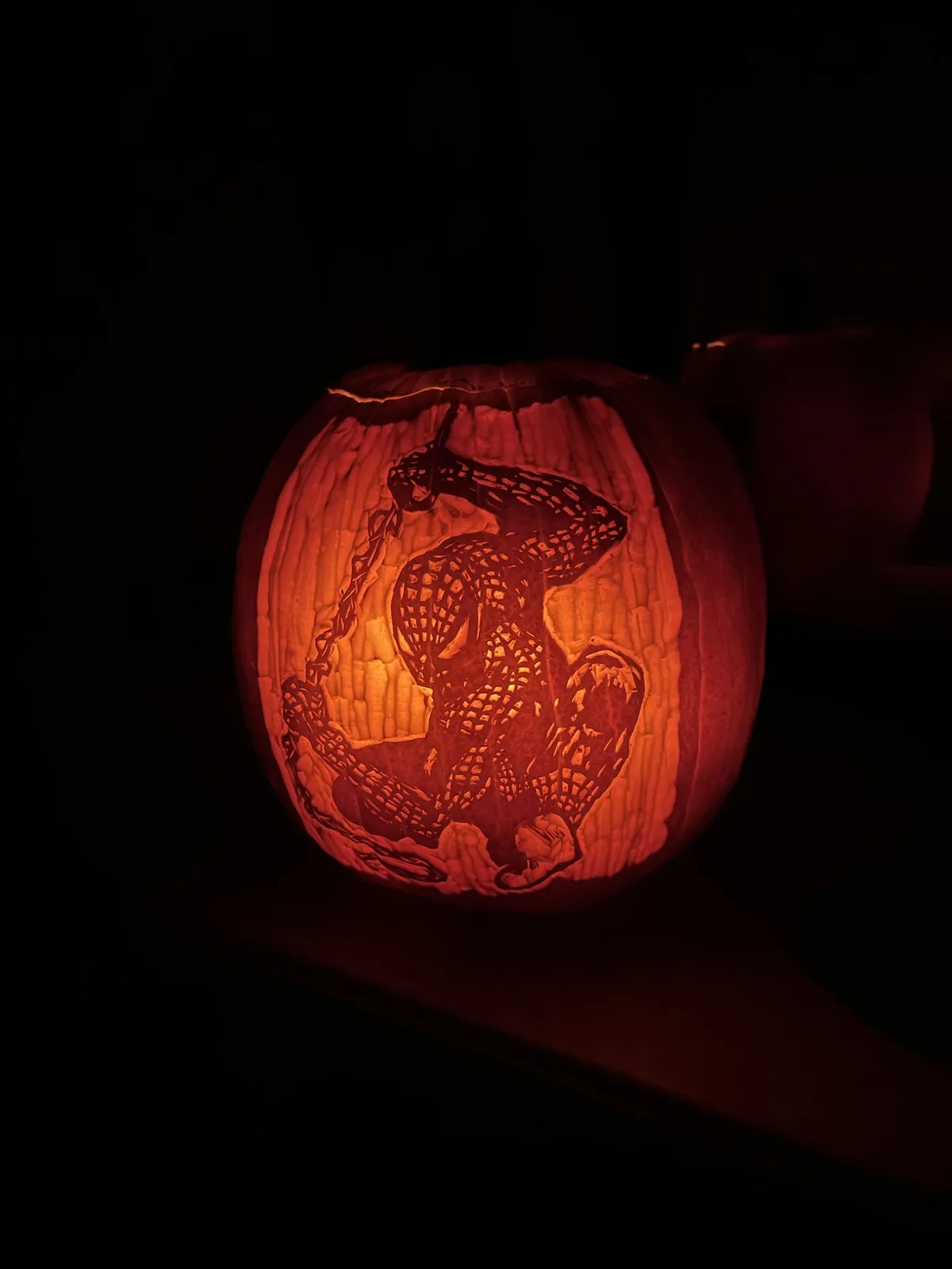 A carved pumpkin illuminated from within, featuring a detailed design of Spider-Man in his classic red and blue suit being…