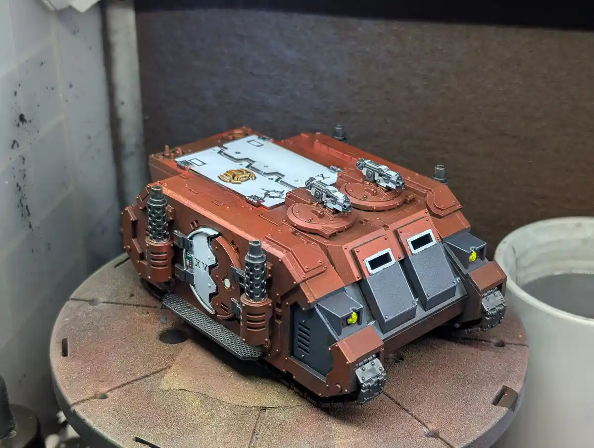 A detailed, painted miniature of a heavily armored, orange-brown futuristic tank with silver and black details sits on a…