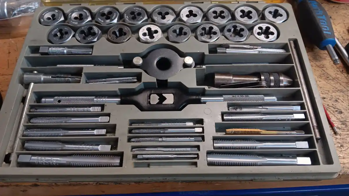An open grey plastic toolbox filled with various metal threading tools, including die heads and taps, neatly arranged in…