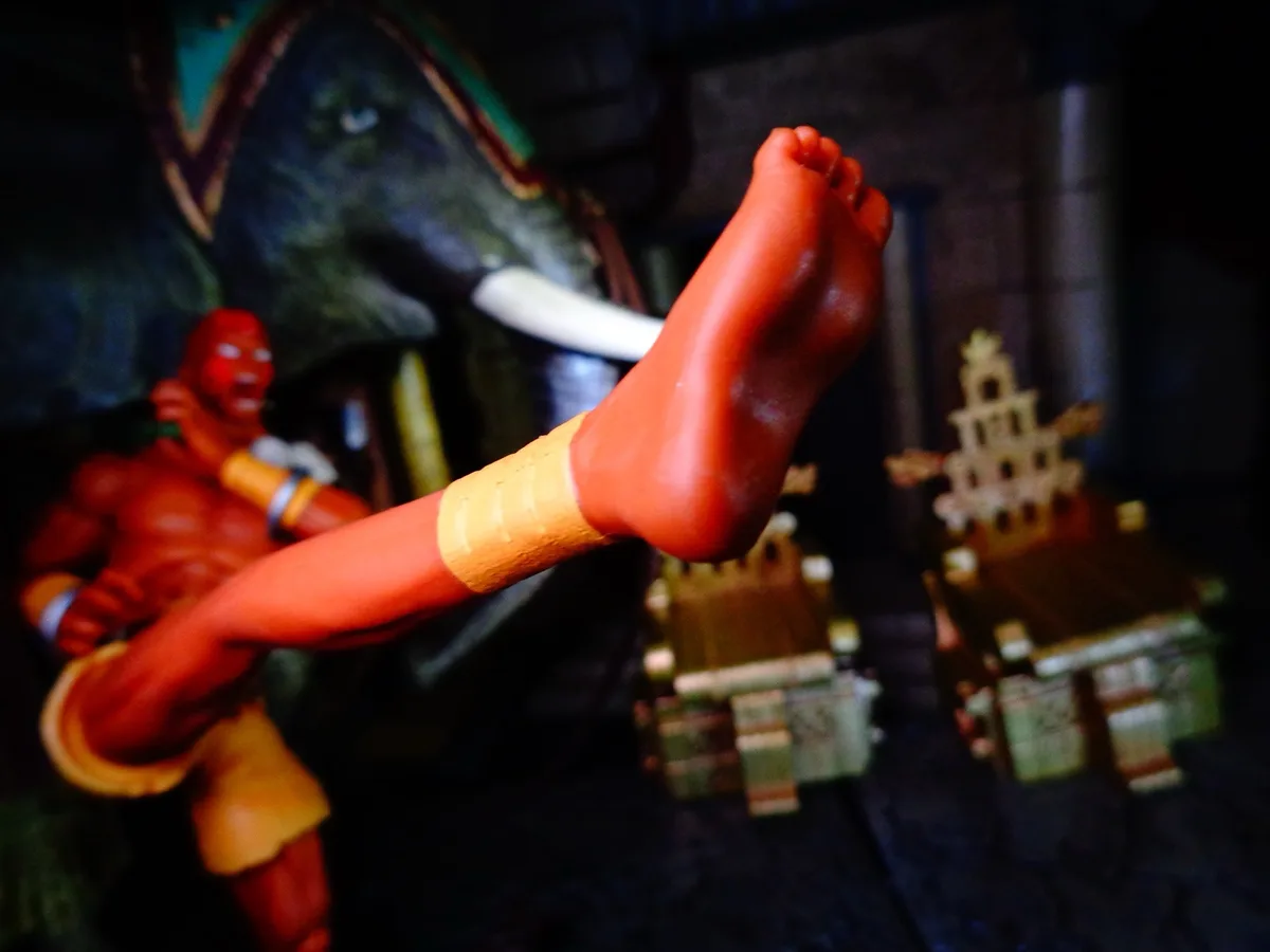 A close-up shot of a red plastic toy figure's bare foot, with a yellow bandage wrapped around the ankle, resting in a…