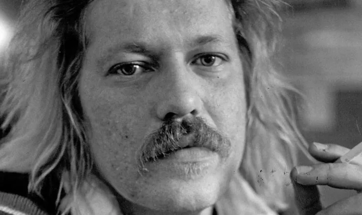 a black and white close-up photo of a man with long hair and a mustache holding a cigarette, with the text 'i'm not a…