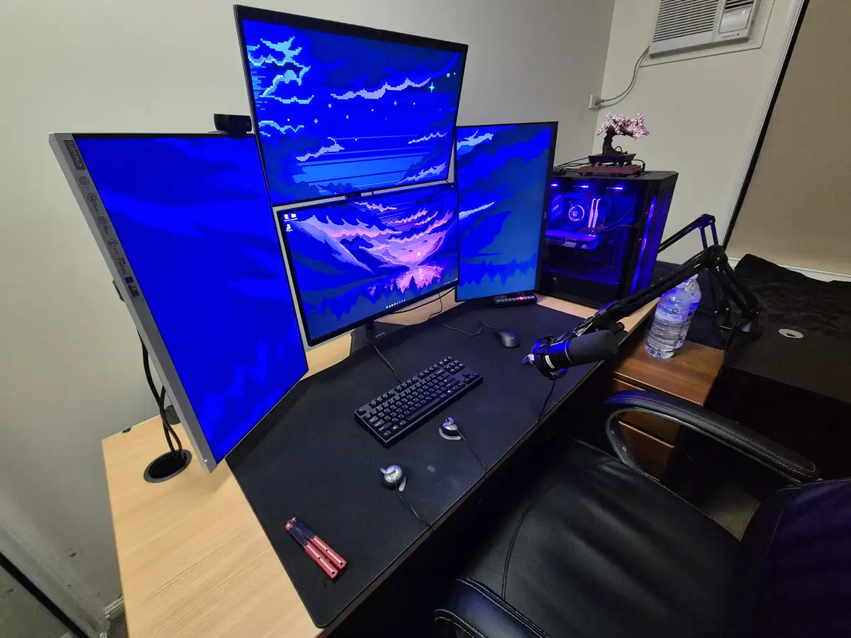 A desk setup with four monitors displaying a blue and purple pixelated landscape wallpaper, a black keyboard, mouse, and…