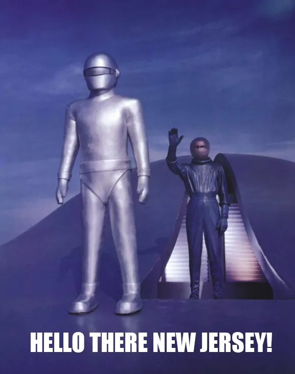 Two silver humanoid figures stand on a futuristic platform under a purple sky; one is tall and still, the other waves from a…