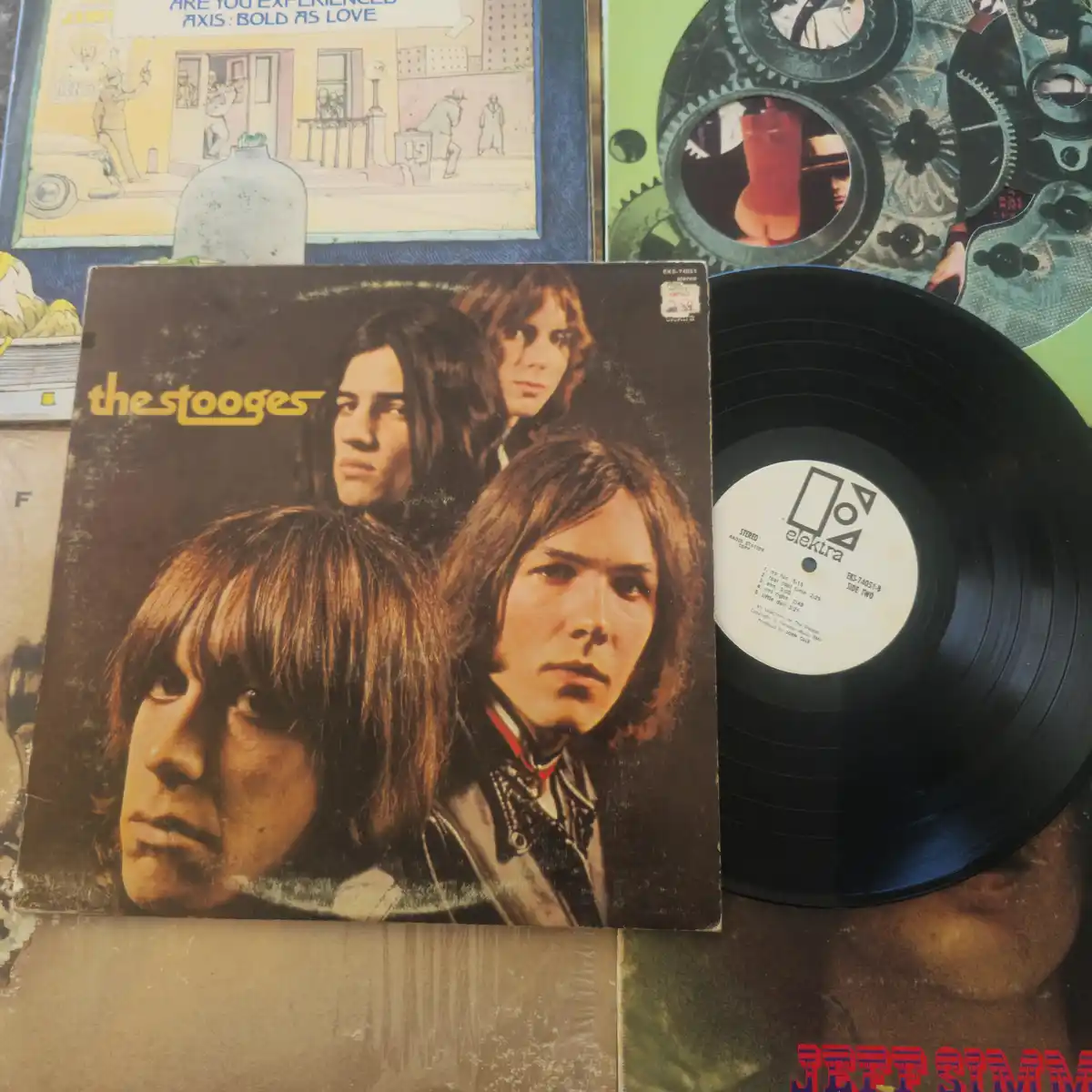A photo shows a vintage vinyl record of The Stooges with its cover and the black disc partially pulled out, revealing the…