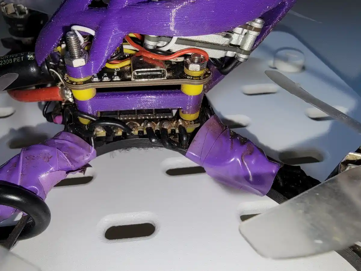 A close-up photo shows the internal components of a drone, featuring purple 3D-printed parts, wires, a USB port, and a…
