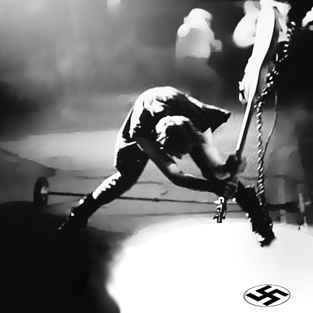 A black and white photo shows a musician on stage bent over, playing a guitar with a swastika symbol overlaid in the bottom…