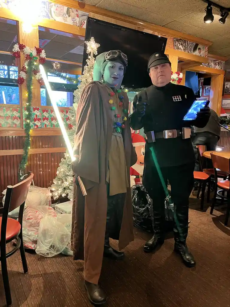 Two people dressed as Star Wars characters, one as a Jedi with a glowing white lightsaber and the other as an Imperial…