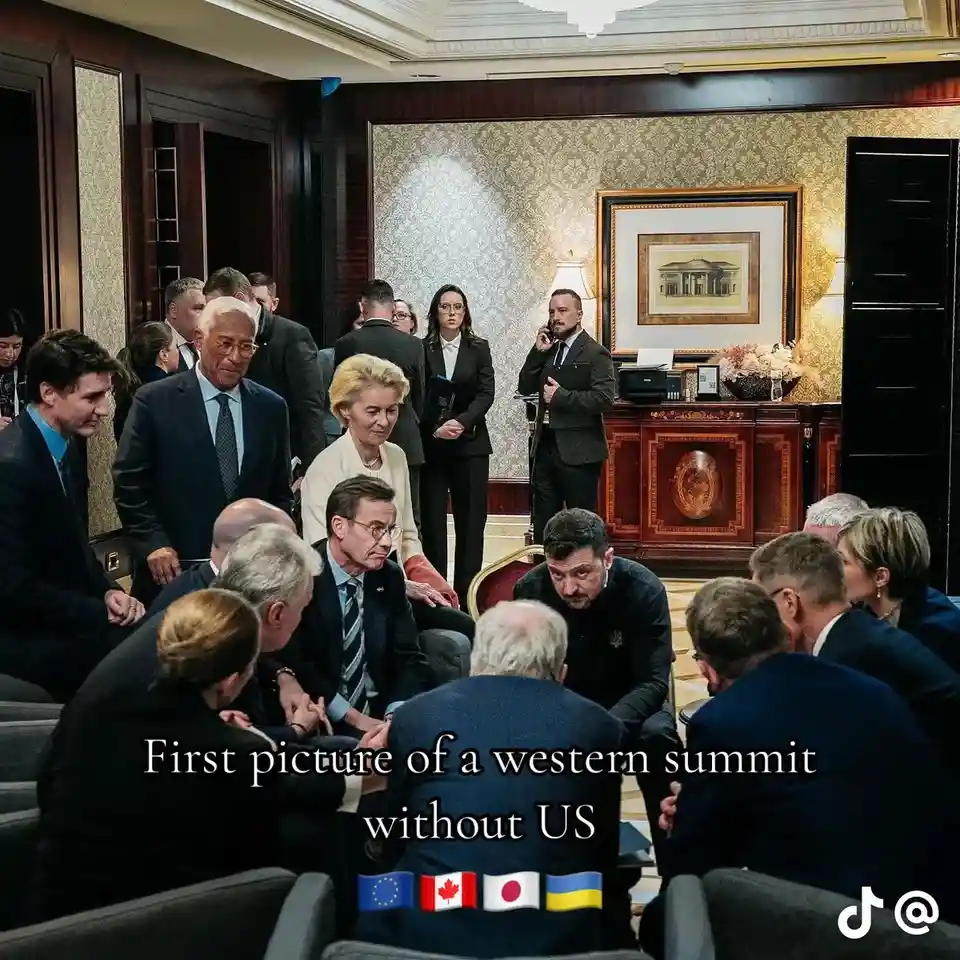 A group of world leaders in formal attire are gathered in an ornate, wood-paneled room with patterned wallpaper and a large…