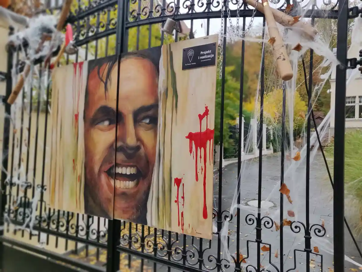 A large, painted portrait of a man with a screaming, bloodied expression is mounted on a black wrought-iron gate decorated…
