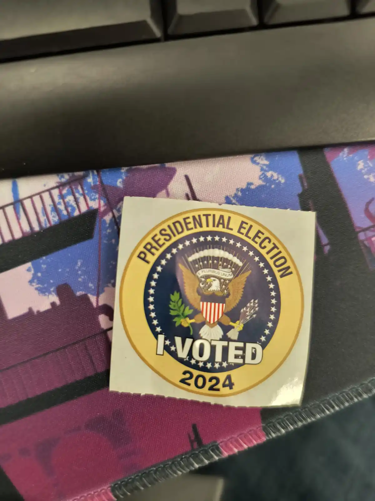 A close-up photo shows a 2024 U.S. presidential election 'I VOTED' sticker, featuring the Great Seal of the United States…