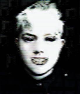 A heavily pixelated, black-and-white image of a person with short hair, dark eye makeup, and a wide, toothy grin. The image…