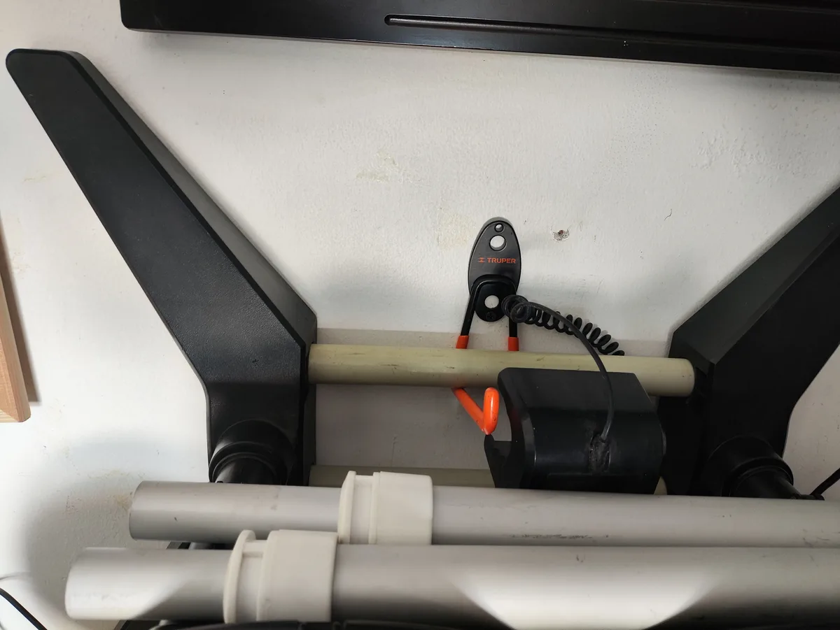 A close-up photo shows a black and orange Truper brand tool mounted on a white wall, clipped to a horizontal beige pipe…