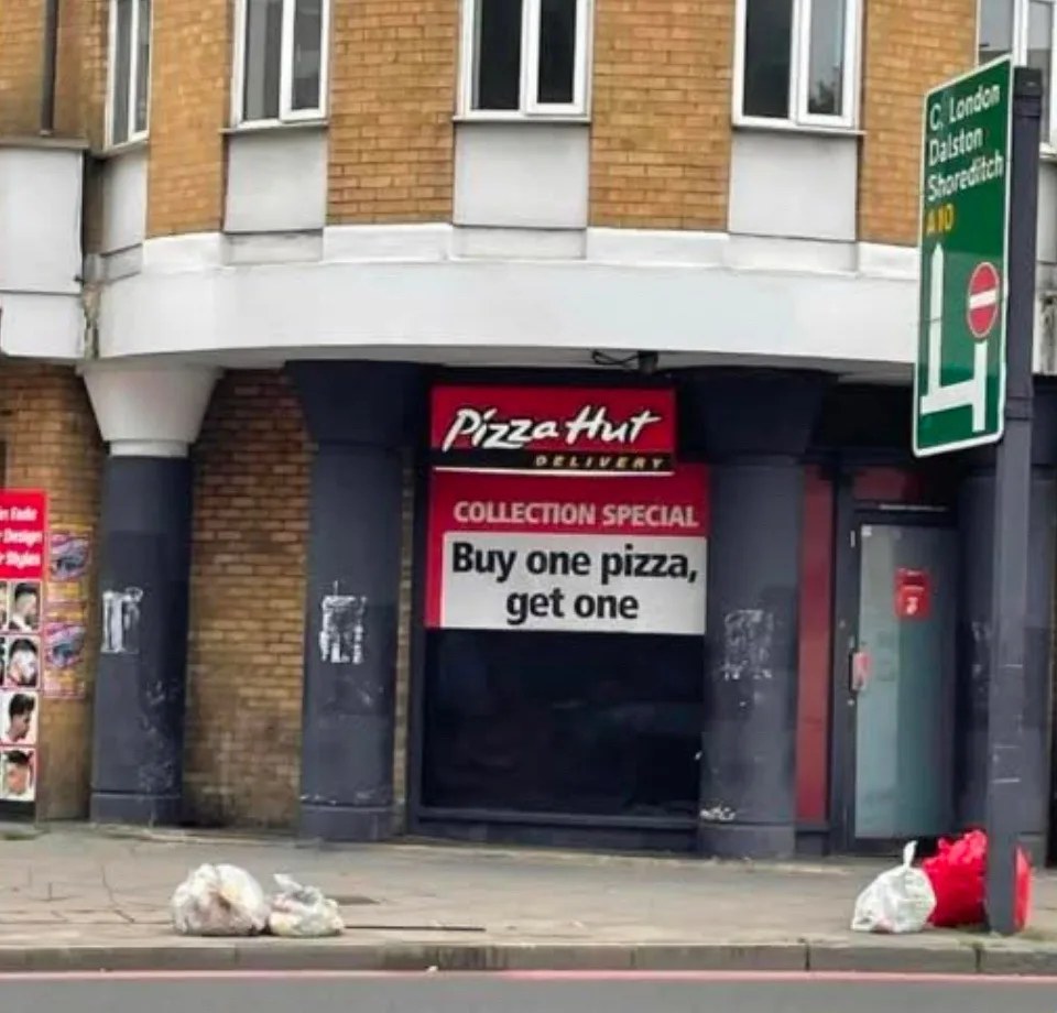 A Pizza Hut storefront with a red sign advertising a 'Collection Special: Buy one pizza, get one'. The building is brick…
