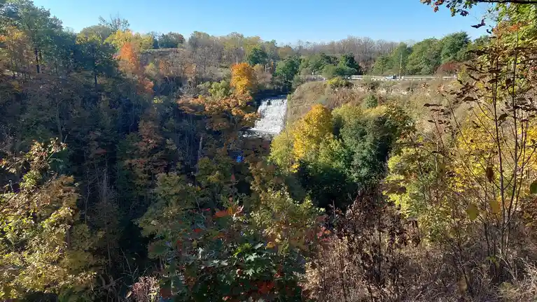 A scenic autumn photo shows a waterfall cascading through a forest with trees displaying vibrant yellow, orange, and green…