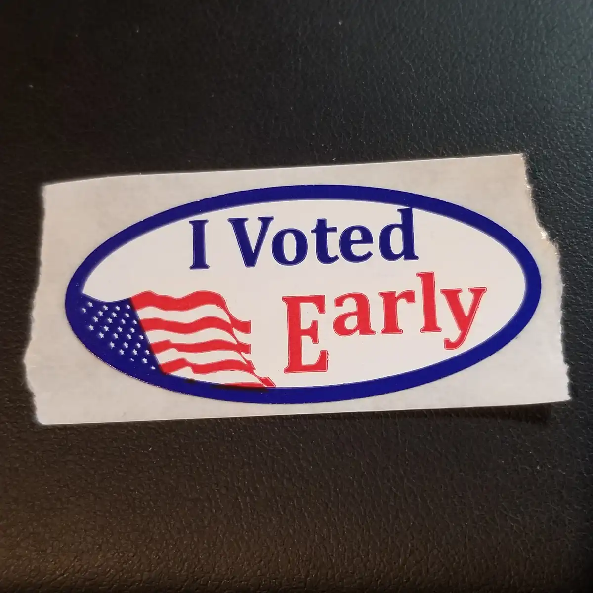 A close-up photo shows a rectangular sticker with a blue oval border on a white background, placed on a dark textured…