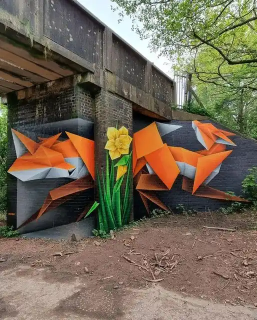 A vibrant mural on a brick wall under an overpass depicts two stylized orange and white foxes in origami-like geometric…