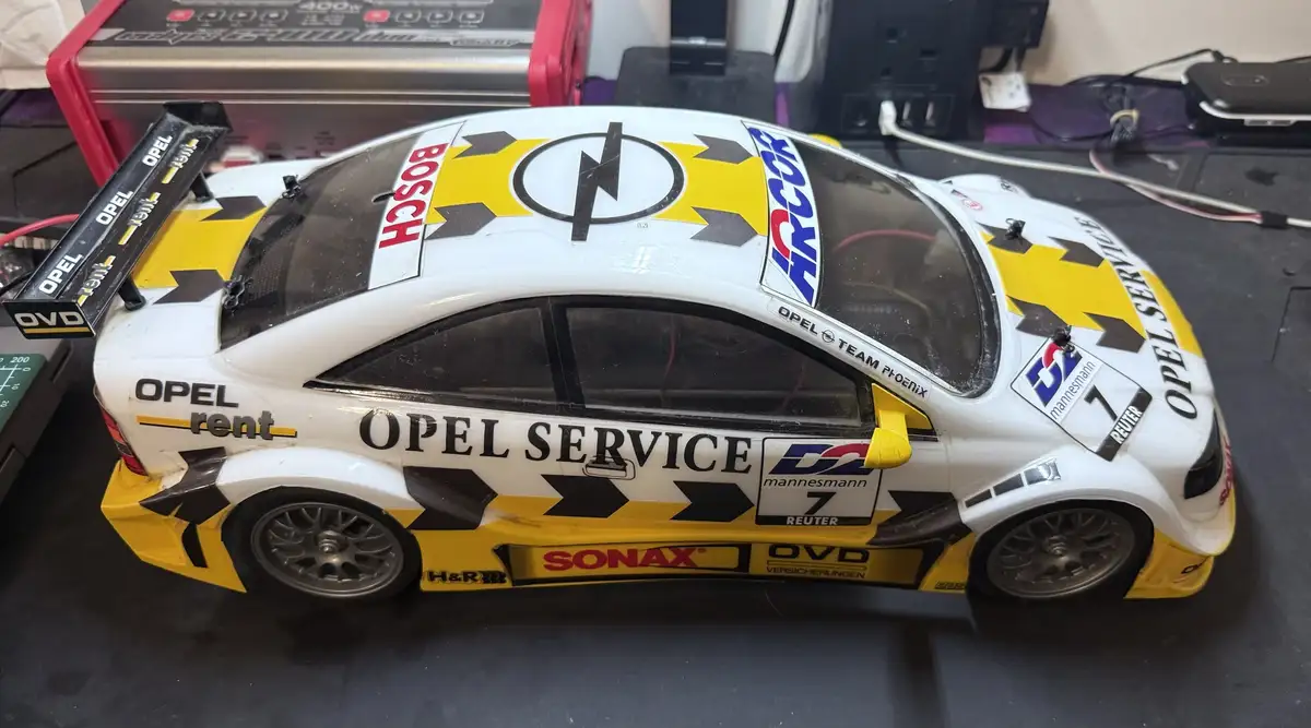A white and yellow scale model race car with 'OPEL SERVICE' and sponsor logos like Bosch, Mannesmann, and Sonax is shown on…