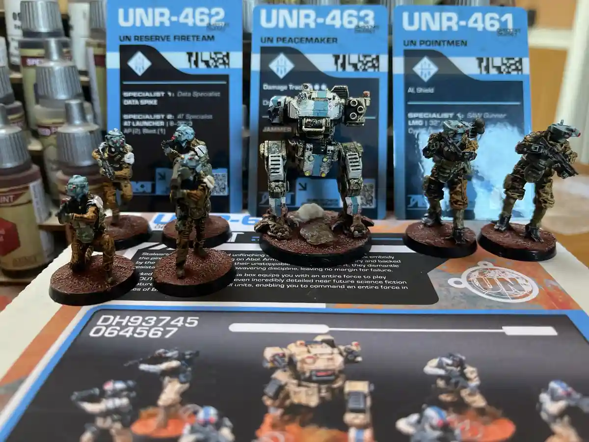 A photo of painted miniature sci-fi soldiers and a mech on display with their corresponding game cards labeled UNR-462…