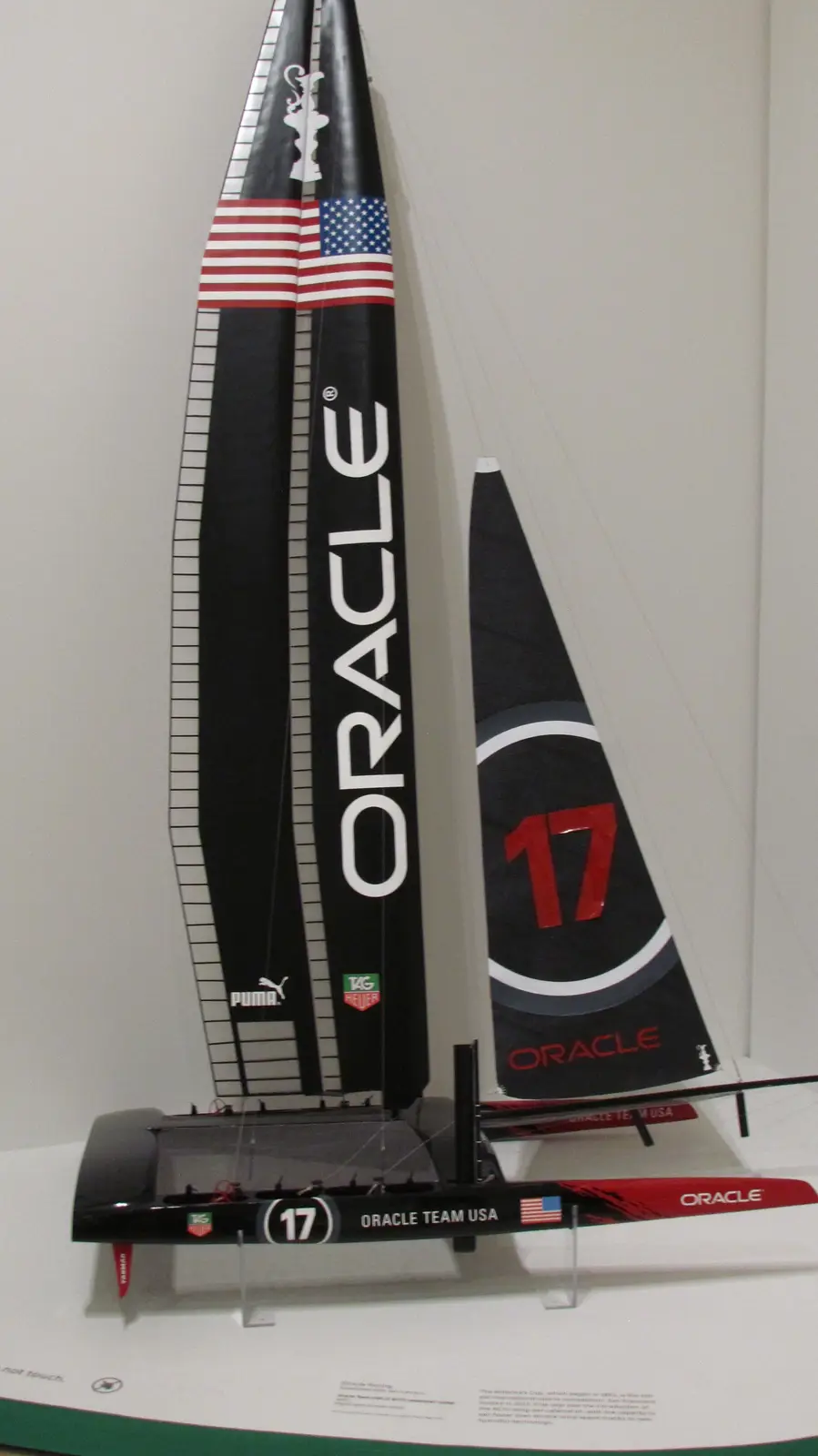 A museum display of a scale model of the Oracle Team USA racing sailboat, marked with number 17 and American flag motifs…