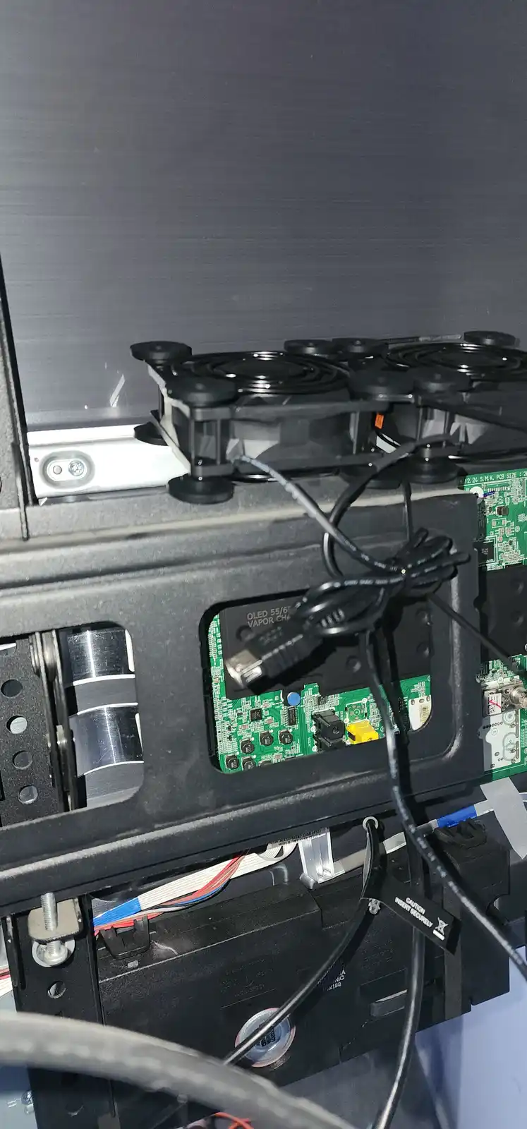 A close-up photo of the internal components of a vaping device, showing a green circuit board with a USB cable plugged into…