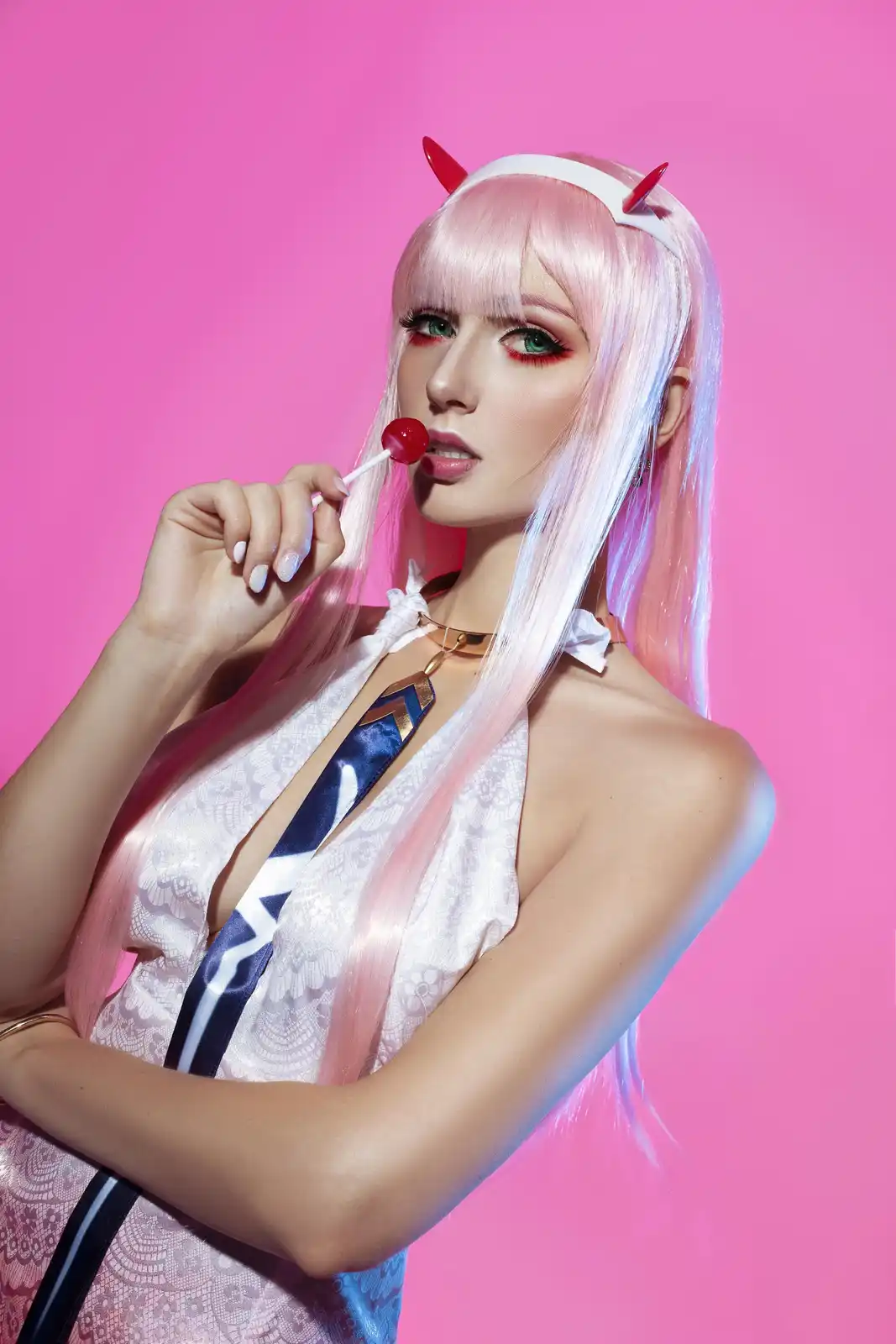 A person in cosplay as the anime character Aya from 'Kaguya-sama: Love is War' poses against a solid pink background…