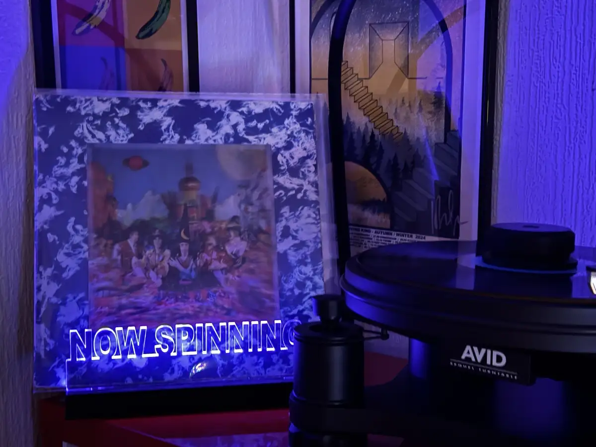 A vinyl record player with an 'AVID SEQUEL FUSITABLE' turntable sits beside a glowing 'NOW_SPINNING' sign, which is placed…