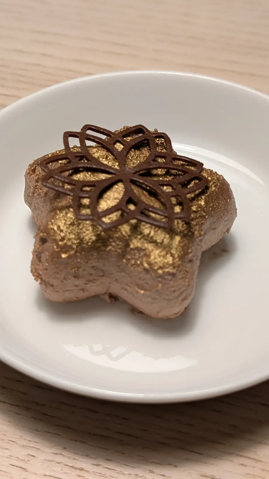 a close-up photo shows a star-shaped chocolate dessert on a white plate, covered in gold leaf and topped with a delicate…