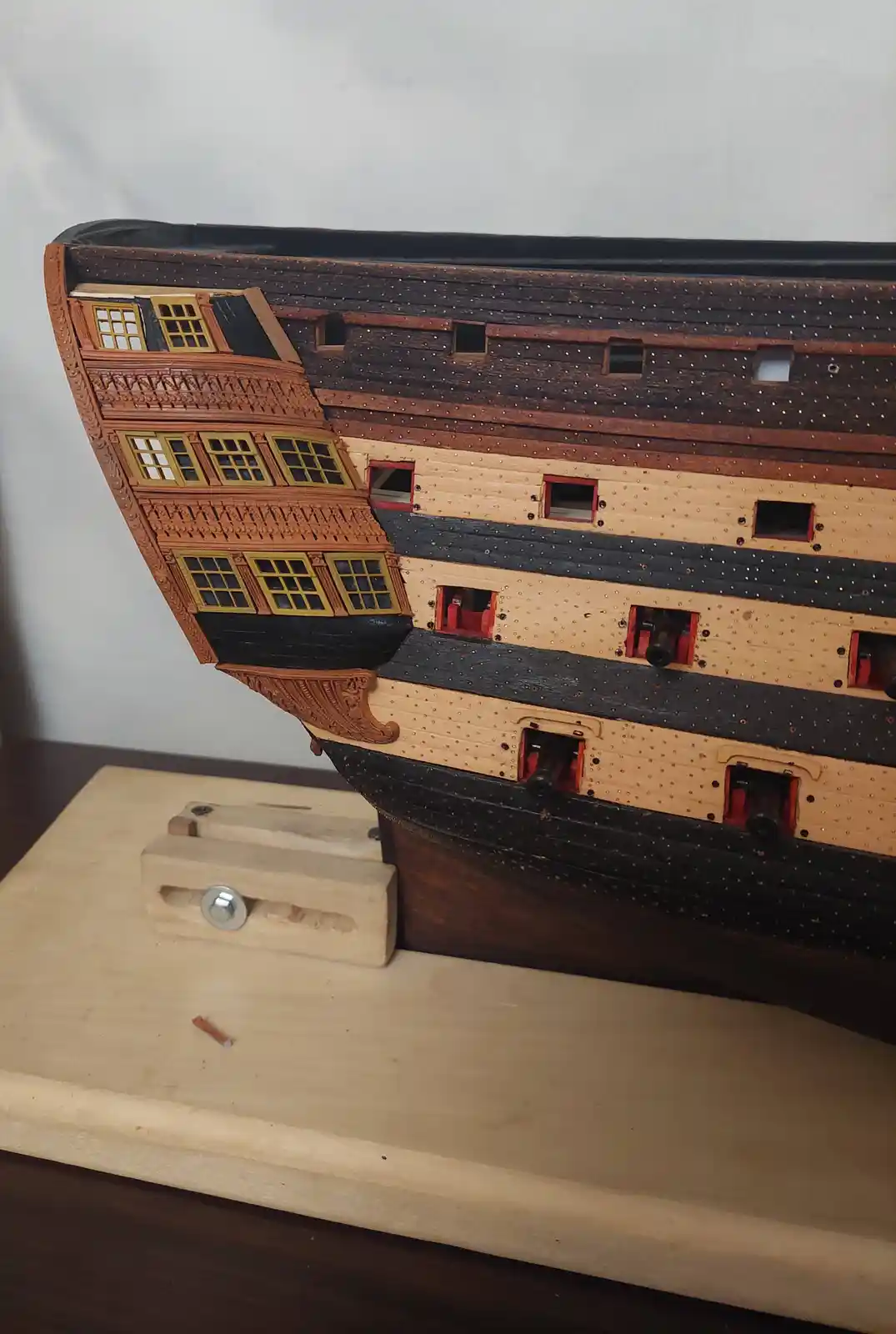 A highly detailed wooden model of a historical multi-deck sailing ship, featuring intricate carvings, painted windows, and…