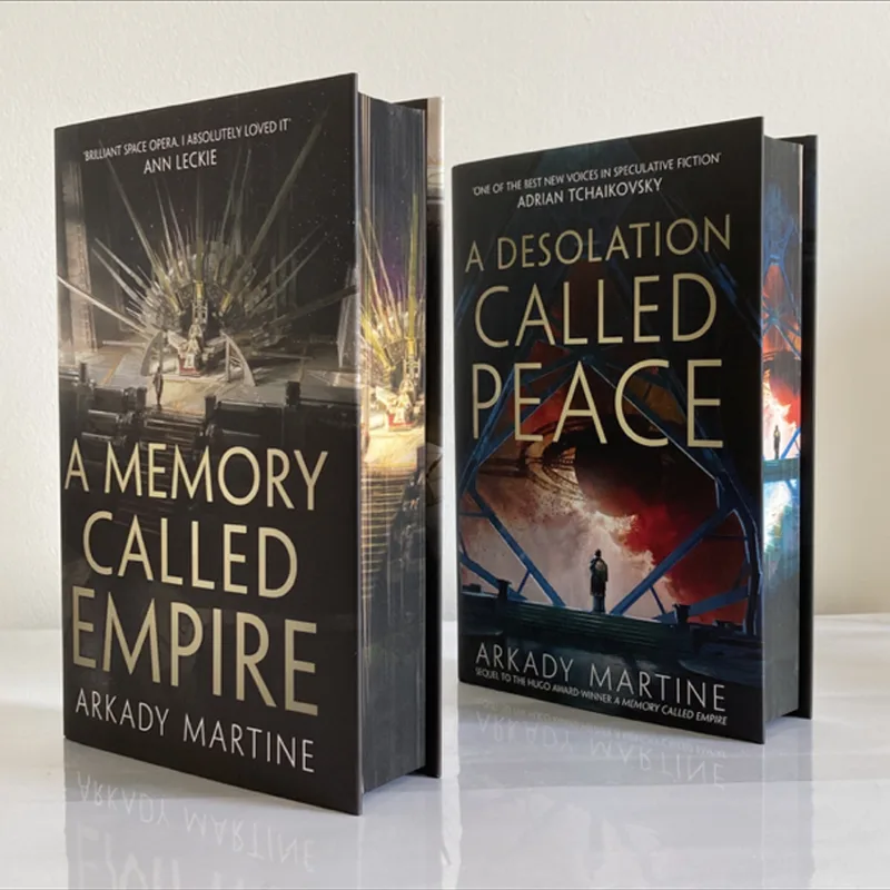 Two hardcover books by Arkady Martine, 'A Memory Called Empire' and its sequel 'A Desolation Called Peace', stand upright on…