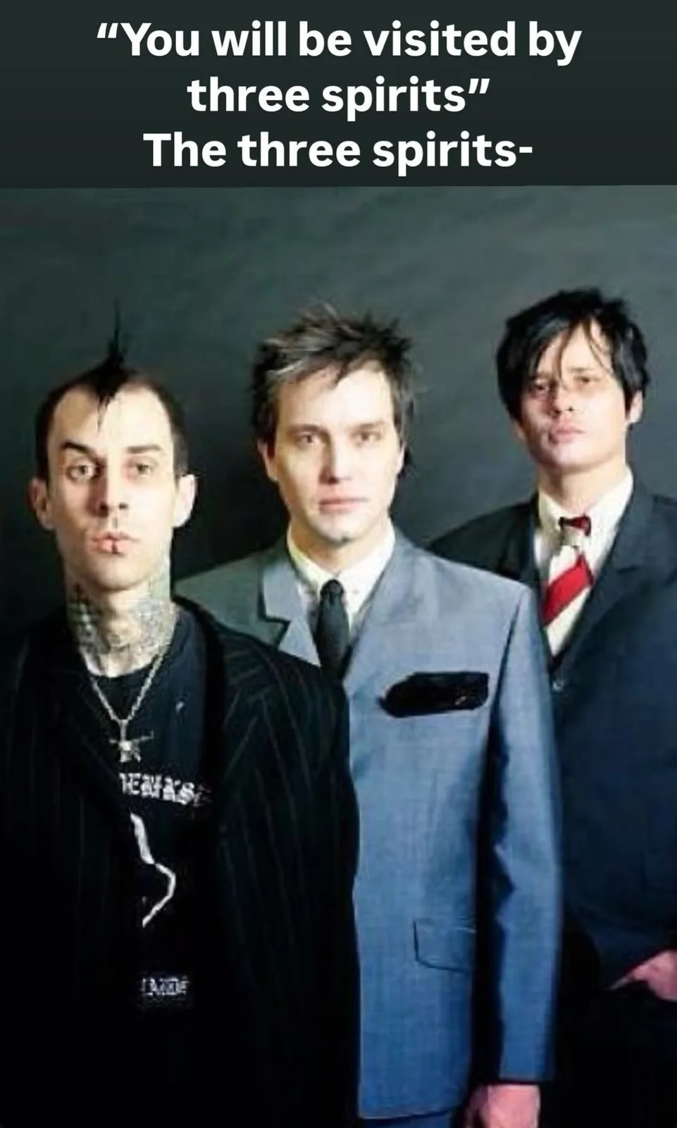 Three men stand in a row against a dark background. The man on the left has tattoos on his neck, a mohawk, and a lip…