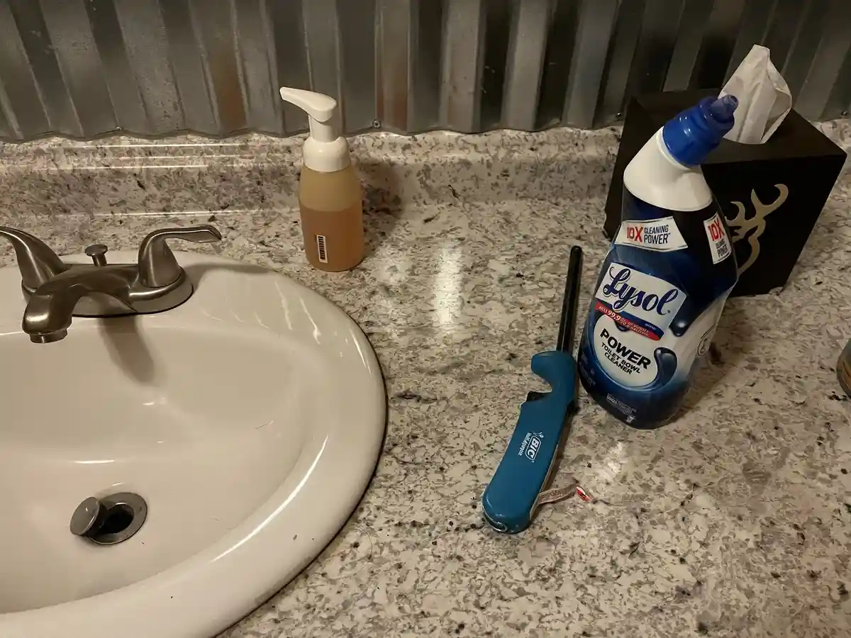 A bathroom countertop next to a sink has a bottle of Lysol Power Toilet Bowl Cleaner, a blue BIC pen, and a tissue box. The…