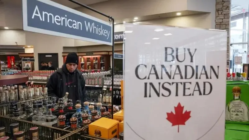 A man in a black beanie and hoodie stands in a liquor store aisle under a sign reading 'American Whiskey'. A large white…