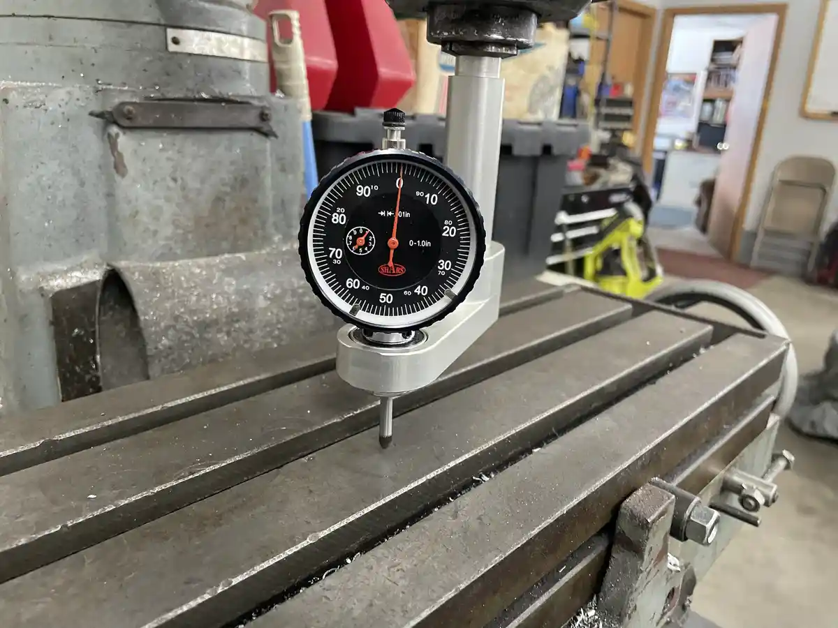 A close-up photo of a precision dial indicator mounted on a metal milling machine, its needle pointing to zero on a scale…