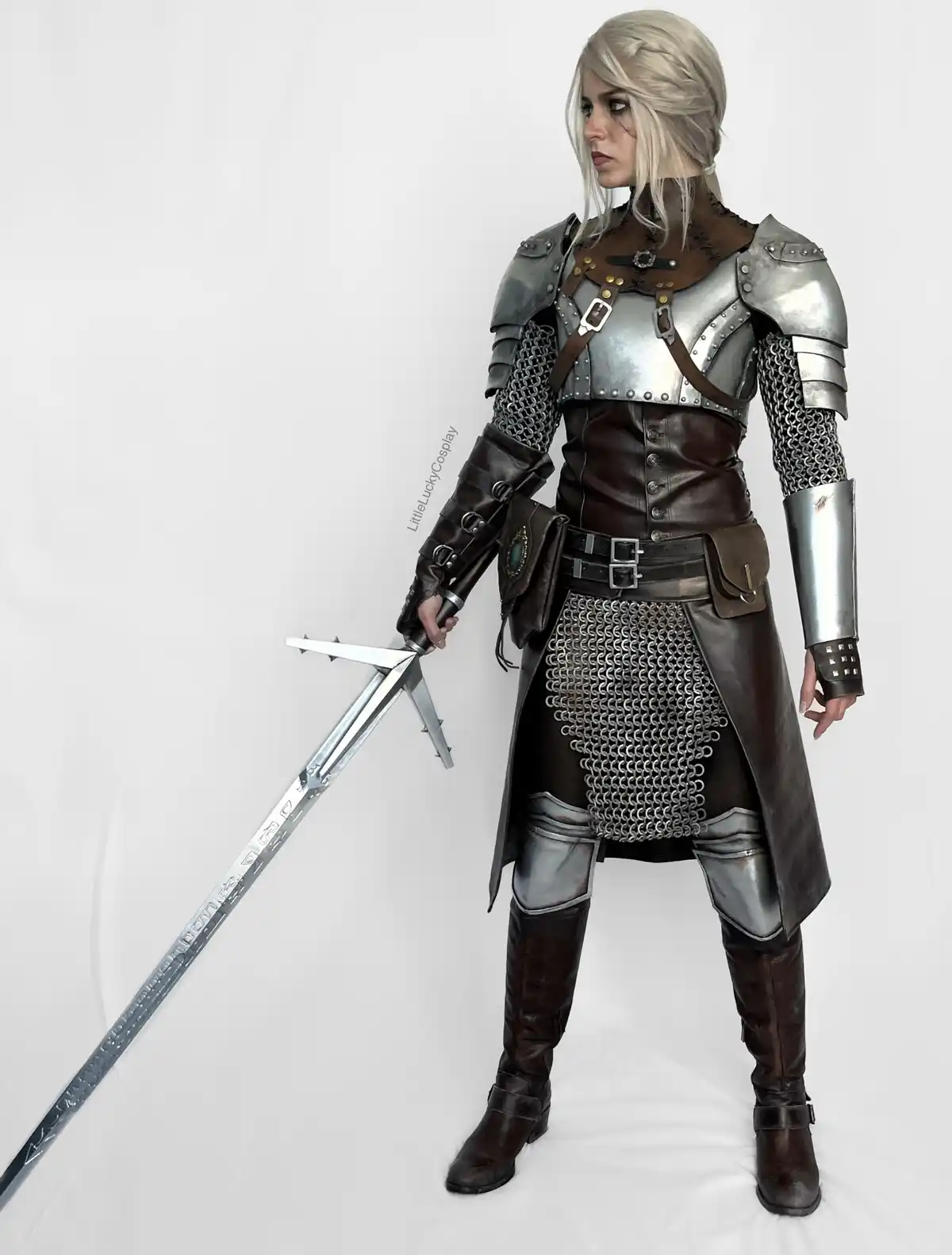 A person in a detailed cosplay of Geralt of Rivia from The Witcher, wearing silver and brown armor, chainmail, and holding a…