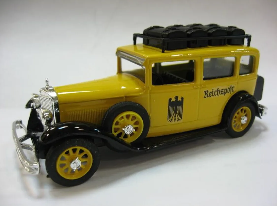 A yellow vintage toy car model with black trim, featuring the word 'Reichspost' and a black eagle emblem on its side, with a…