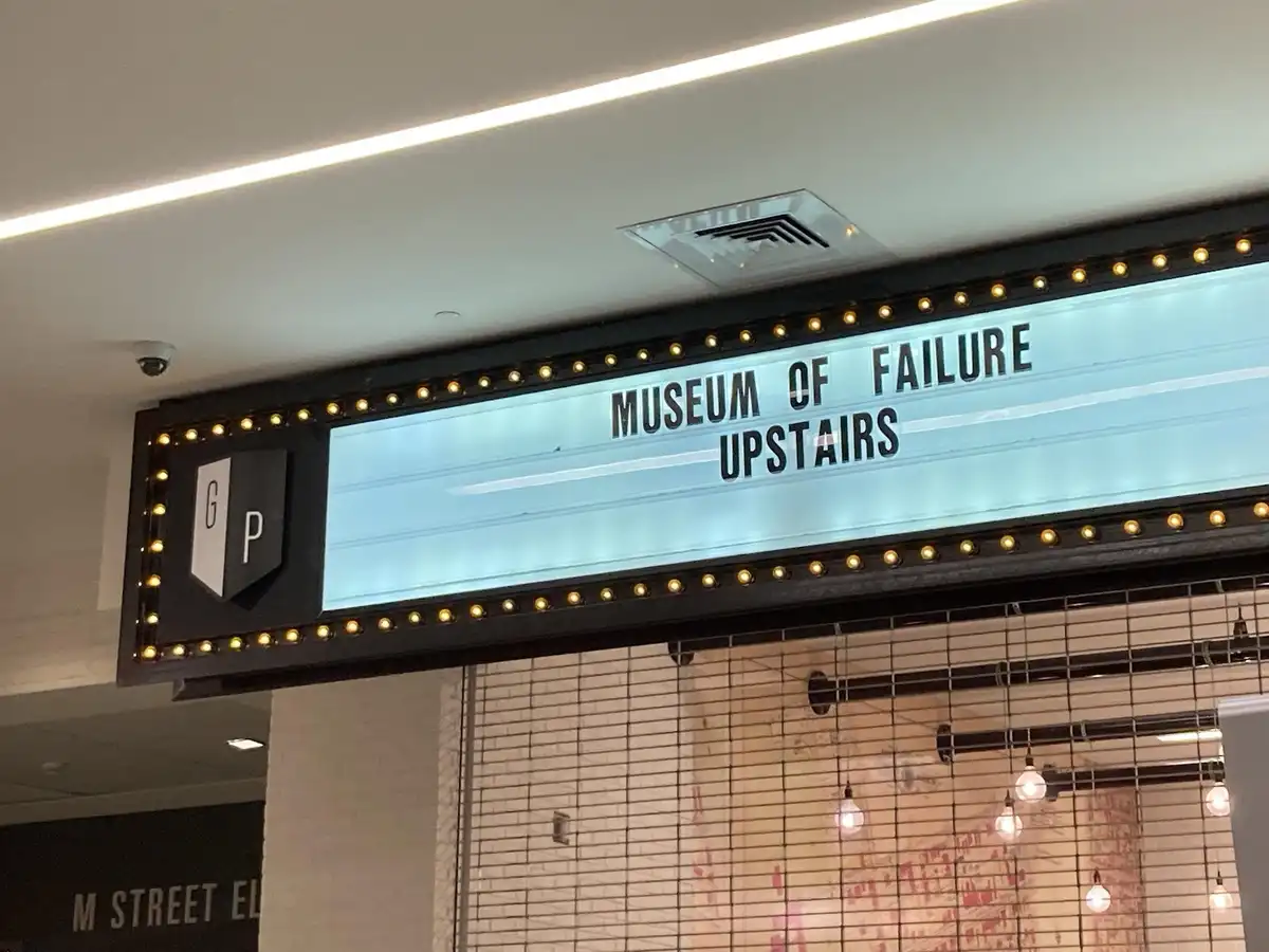 A lit-up marquee sign with black lettering on a light blue background reads 'MUSEUM OF FAILURE' on the top line and…