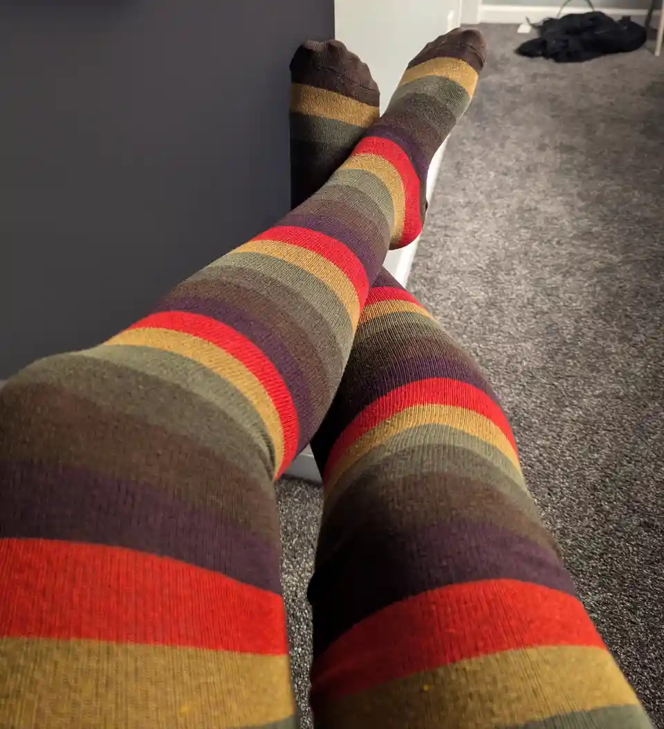 A close-up photo shows a person's legs wearing colorful, horizontally striped socks with red, yellow, green, and purple…
